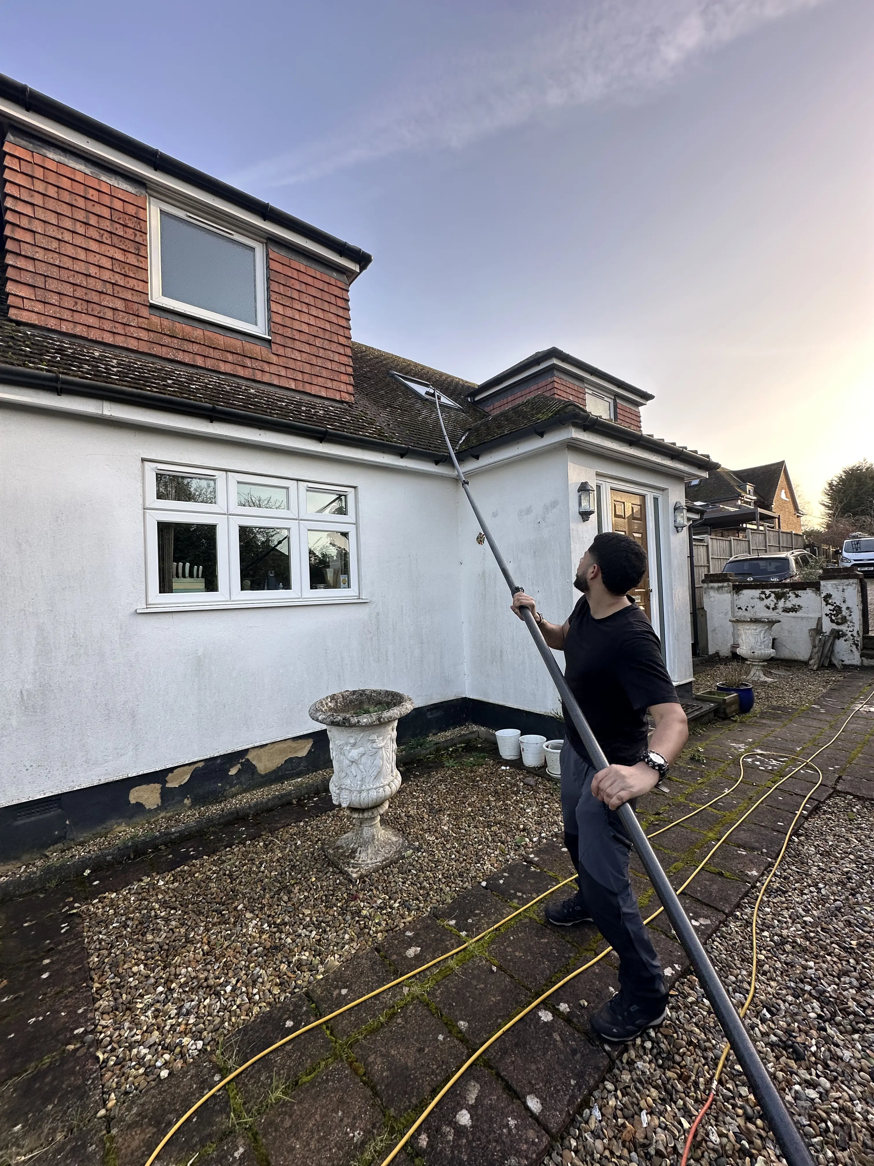 Cleaning an upstairs window of a house with a water-fed pole from ground level.