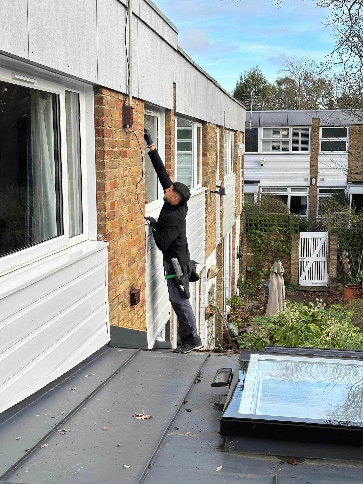 Cleaning upper-floor windows standing on a flat roof, beside a glazed roof lantern.