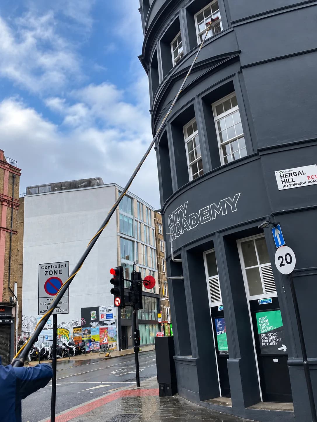 Reaching the upper windows of a curved building with a water-fed pole.